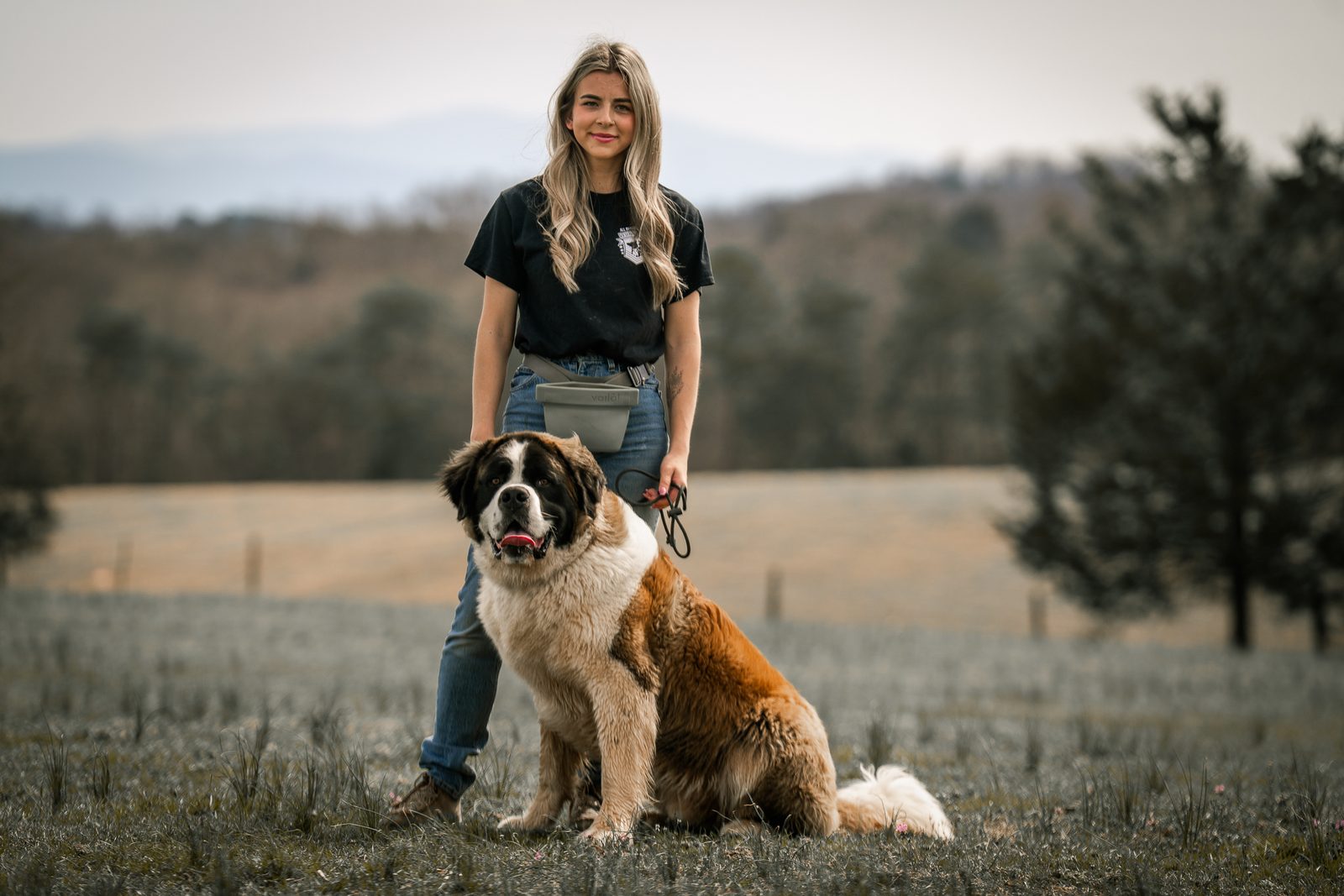 A woman standing in a field with a large dog seated beside her